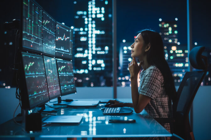 Portrait of a Financial Analyst Working on Computer with Multi Monitor Workstation with Real Time Stocks, Commodities and Exchange Market Charts. Businesswoman at Work in Investment Broker Agency.