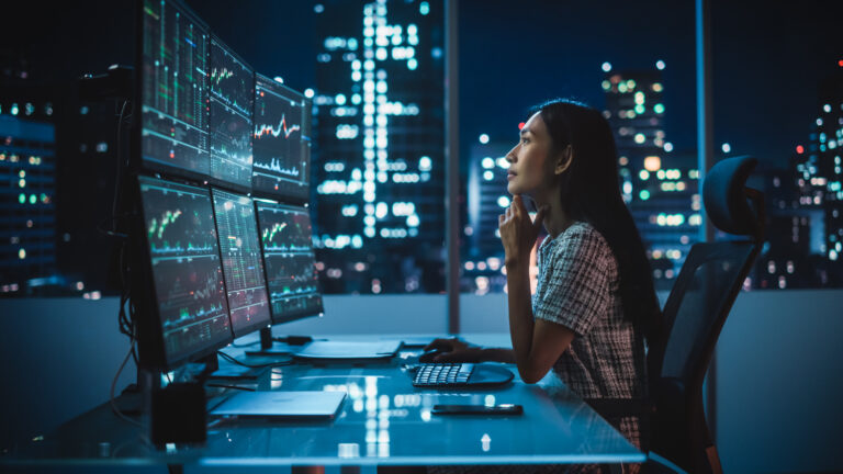 Portrait of a Financial Analyst Working on Computer with Multi Monitor Workstation with Real Time Stocks, Commodities and Exchange Market Charts. Businesswoman at Work in Investment Broker Agency.