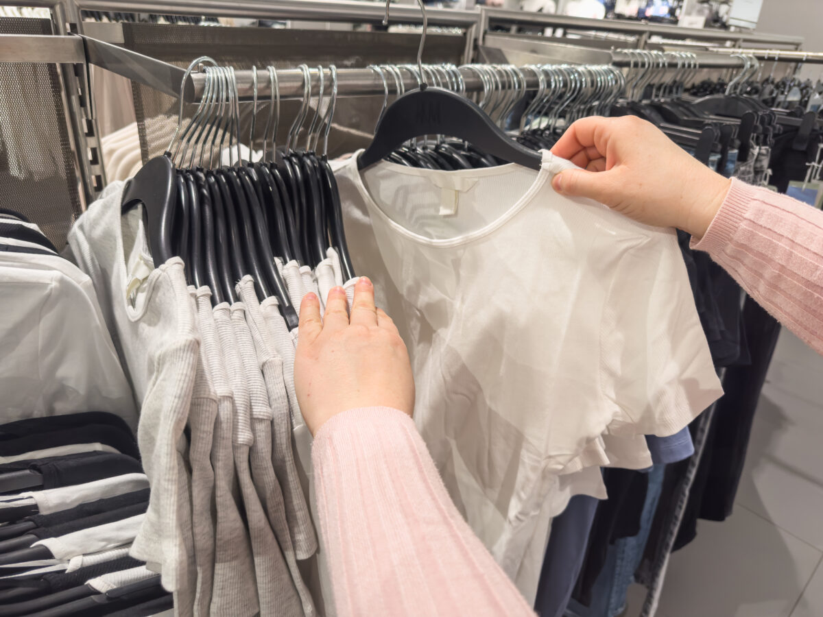 Woman looking through hangers with stylish sweaters in clothing shop
