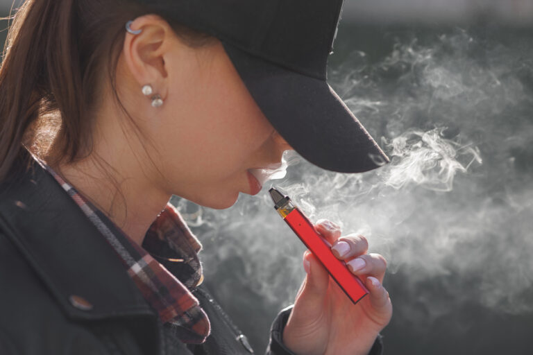 Young girl smokes a vape close up on a dark background, women smoke electronic cigarette in street
