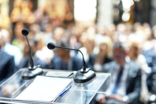 Microphones in focus, unrecognizable people in background at business conference, corporate presentation, workshop, coaching training, news conference, company meeting, public or political event