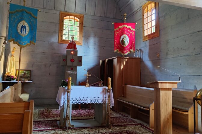 Interiér dreveného kostolíka v Gutech s oltárom, lavicami a liturgickými zástavami, replika postavená v roku 2021 po požiari pôvodnej stavby.