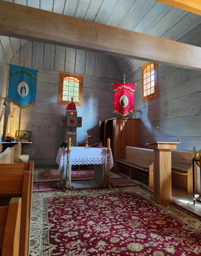 Interiér dreveného kostolíka v Gutech s oltárom, lavicami a liturgickými zástavami, replika postavená v roku 2021 po požiari pôvodnej stavby.