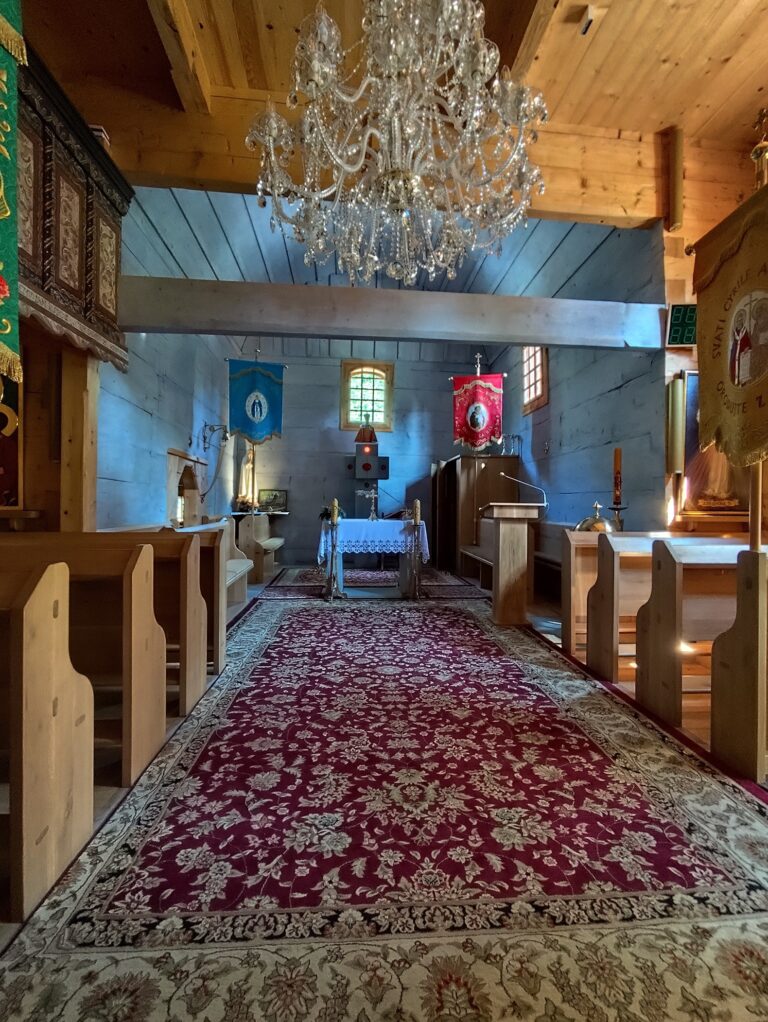 Interiér dreveného kostolíka v Gutech s oltárom, lavicami a liturgickými zástavami, replika postavená v roku 2021 po požiari pôvodnej stavby.