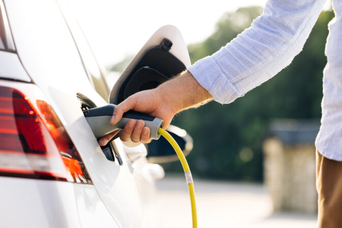 Muž nabíja elektromobil, budúcnosť dopravy sľubuje dlhší dojazd vďaka samoopraviteľným batériám.