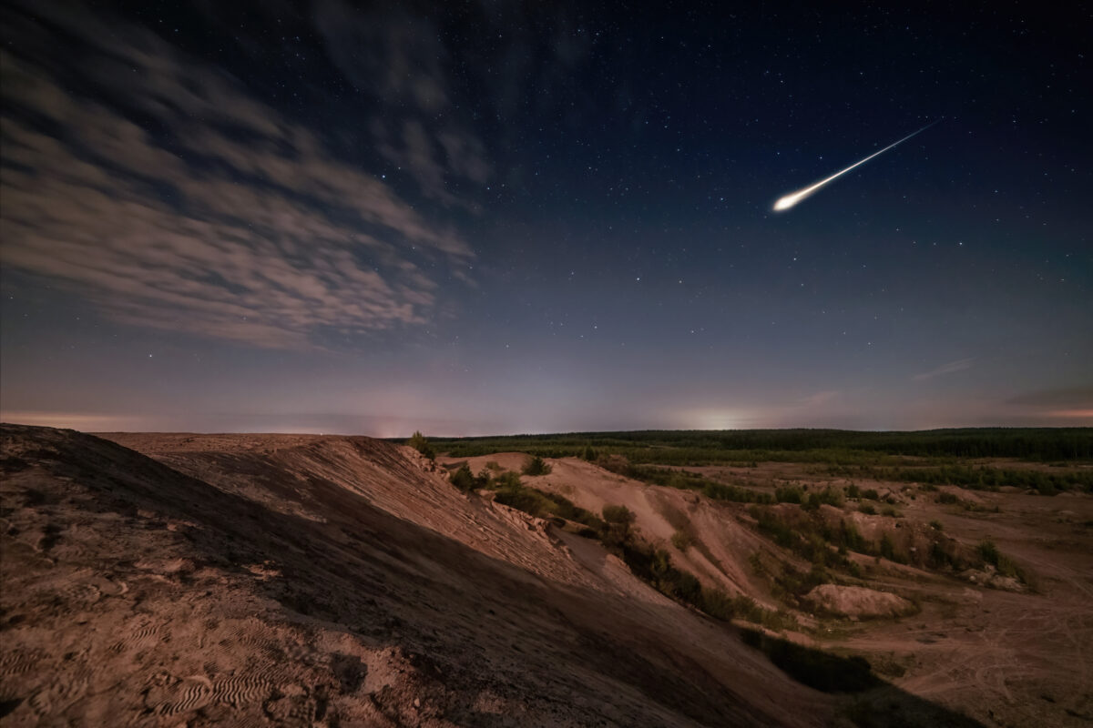 Meteor over sand hills and forest in moon light and starry sky