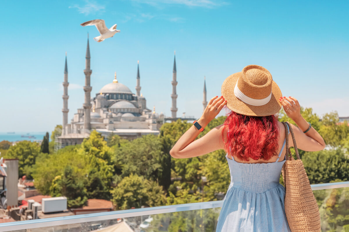 A woman tourist in Istanbul admires the Blue Mosque, with a seagull soaring near the ancient minarets under the summer sky