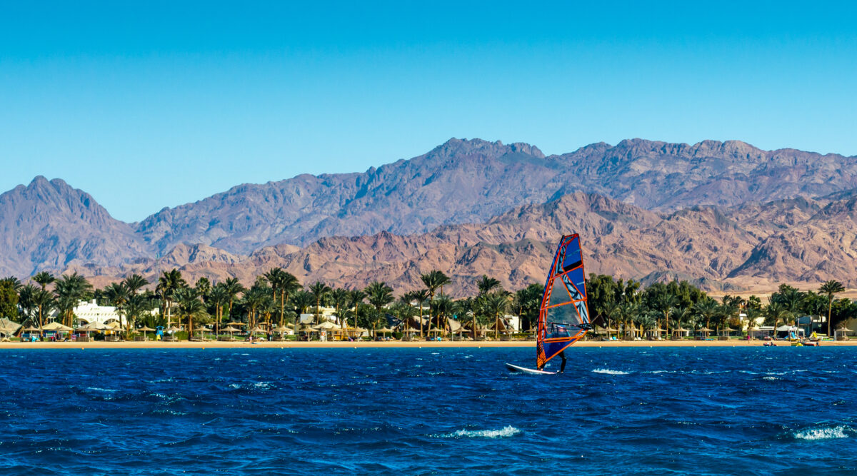Windsurfer rides in the sea on the background of the beach with palm trees and high rocky mountains in Egypt Dahab