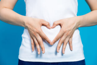 Young woman who makes a heart shape by hands on her stomach.