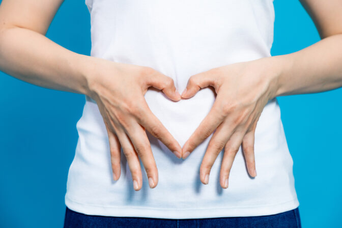 Young woman who makes a heart shape by hands on her stomach.
