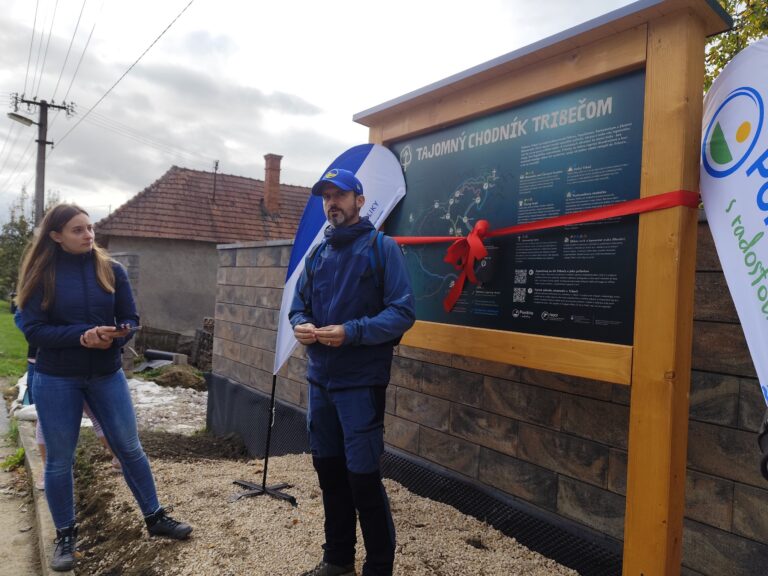 Tajomný chodník Tribečom: Oldo Vaňous, autor šifrovacej hry Stratený v Tribeči, počas otvorenia Tajomného chodníka Tribečom pred informačnou tabuľou so stuhou