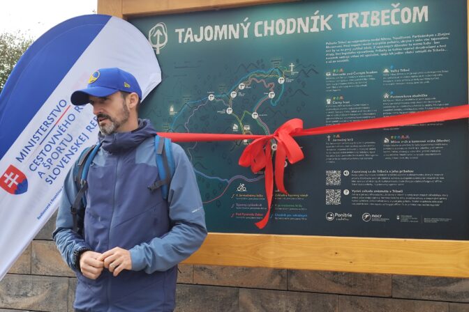 Tajomný chodník Tribečom: Oldo Vaňous, autor šifrovacej hry Stratený v Tribeči, počas otvorenia Tajomného chodníka Tribečom pred informačnou tabuľou so stuhou