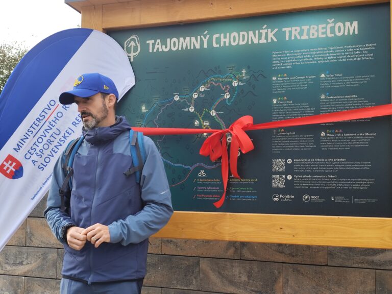 Tajomný chodník Tribečom: Oldo Vaňous, autor šifrovacej hry Stratený v Tribeči, počas otvorenia Tajomného chodníka Tribečom pred informačnou tabuľou so stuhou