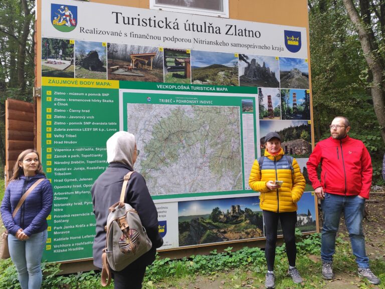Turisti stoja pri veľkoplošnej mape v Turistickej útulni Zlatno s prehľadom trás Tajomného chodníka Tribečom