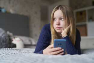 Unhappy Teenage Girl With Mobile Phone Lying On Bed At Home Anxious About Social Media Online Bullying And Using Phone Too Much