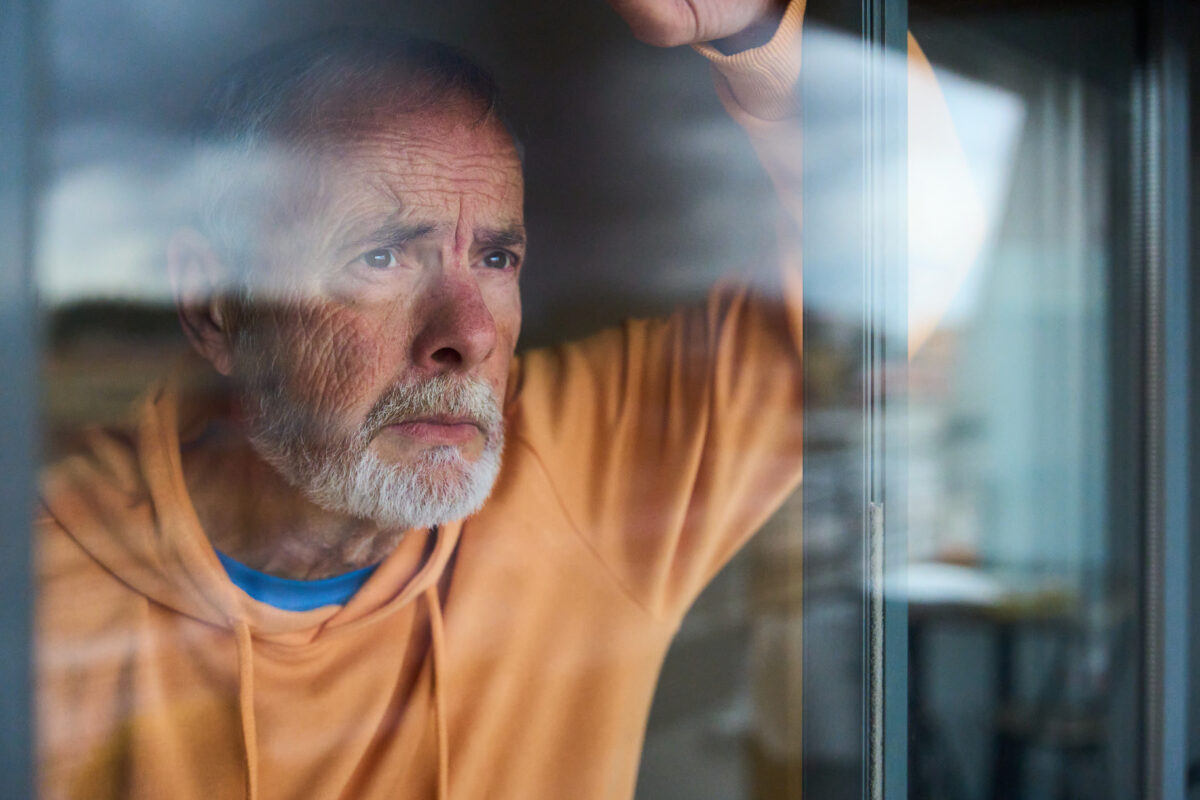 Mature man looking through window with worried expression - mental health, anxiety and depression concept
