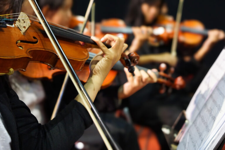 Hands playing violin orchestra with note sheet on stage.