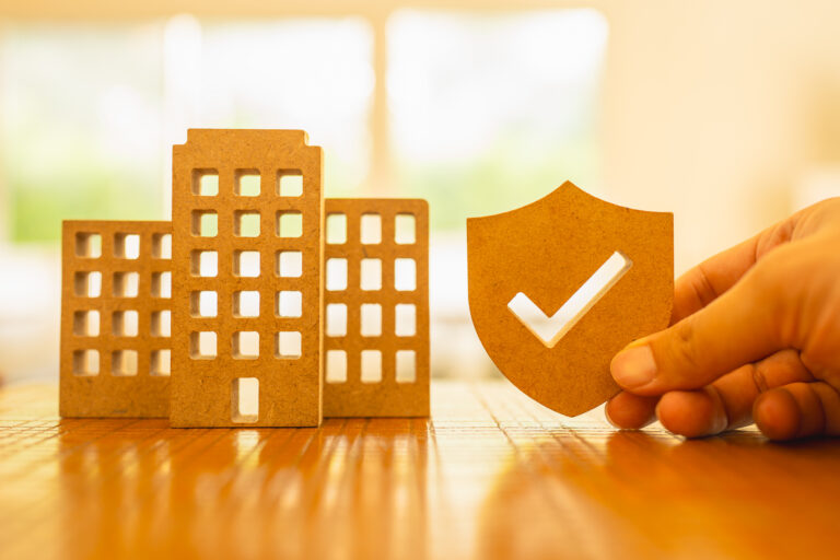 Agent holds insurance symbol next to a company building or condo building model, an idea about getting insurance in a condo or group insurance for company employees.