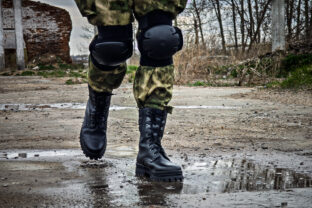 Special forces soldier with an automatic rifle wearing a helmet mask and body armor stands against the background of destroyed buildings. The concept of the army and military exercises.