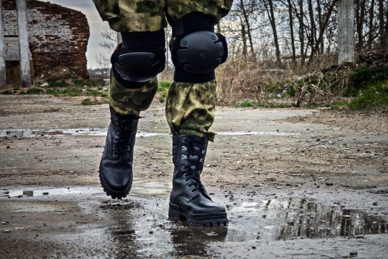 Special forces soldier with an automatic rifle wearing a helmet mask and body armor stands against the background of destroyed buildings. The concept of the army and military exercises.