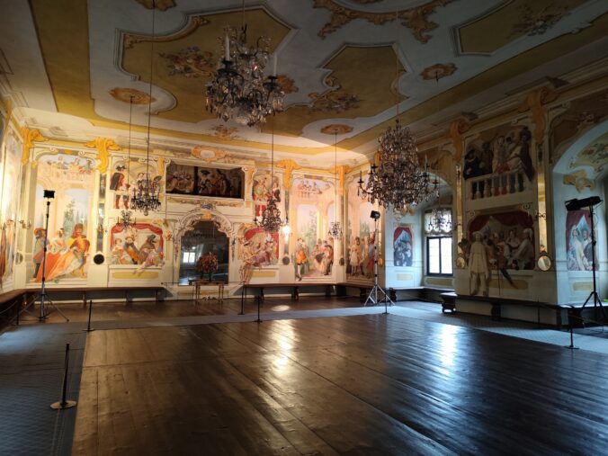 Maškarná sála s freskami Josefa Lederera, zobrazujúcimi postavy v maskách a postavu ducha na stene.