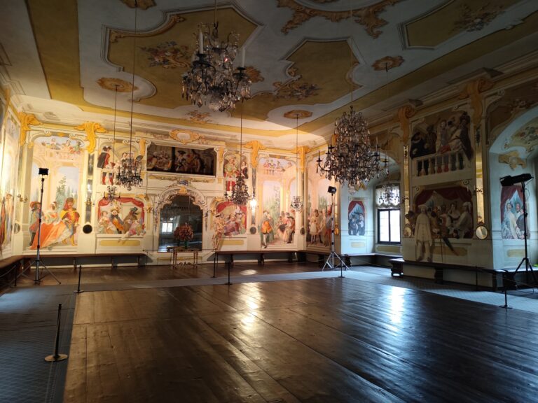 Maškarná sála s freskami Josefa Lederera, zobrazujúcimi postavy v maskách a postavu ducha na stene.