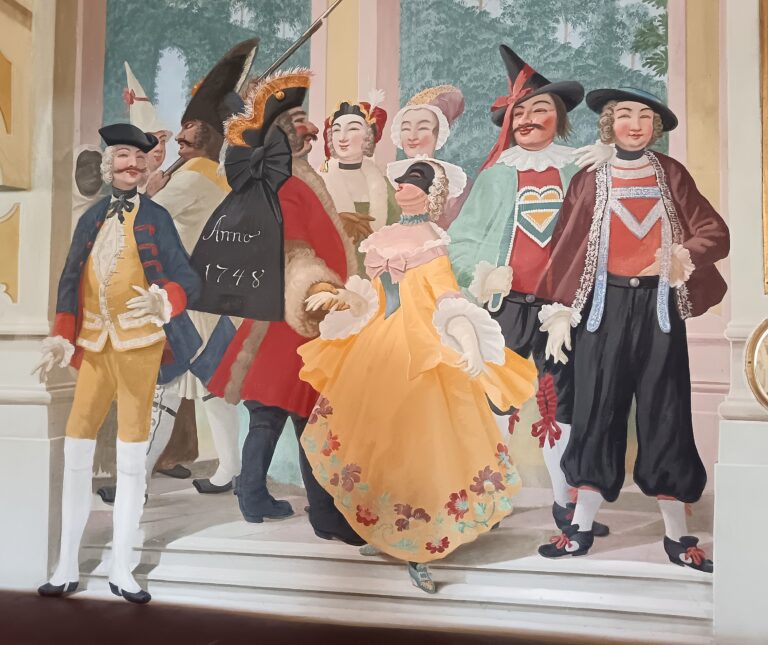 Maškarný sál s freskami Josefa Lederera, zobrazujúcimi postavy v maskách a postavu ducha na stene.