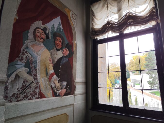 Maškarný sál s freskami Josefa Lederera, zobrazujúcimi postavy v maskách a postavu ducha na stene.