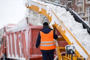 Claw loader vehicle removes snow from the road.  A snowplow pours snow into a truck