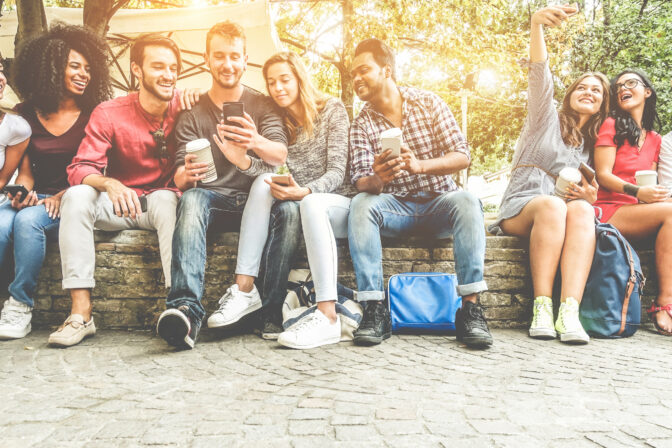 Group of happy friends using smartphones for taking photos and watching videos - Teenagers having fun outdoor with technology trends - Youth and friendship concept - Main focus on center faces