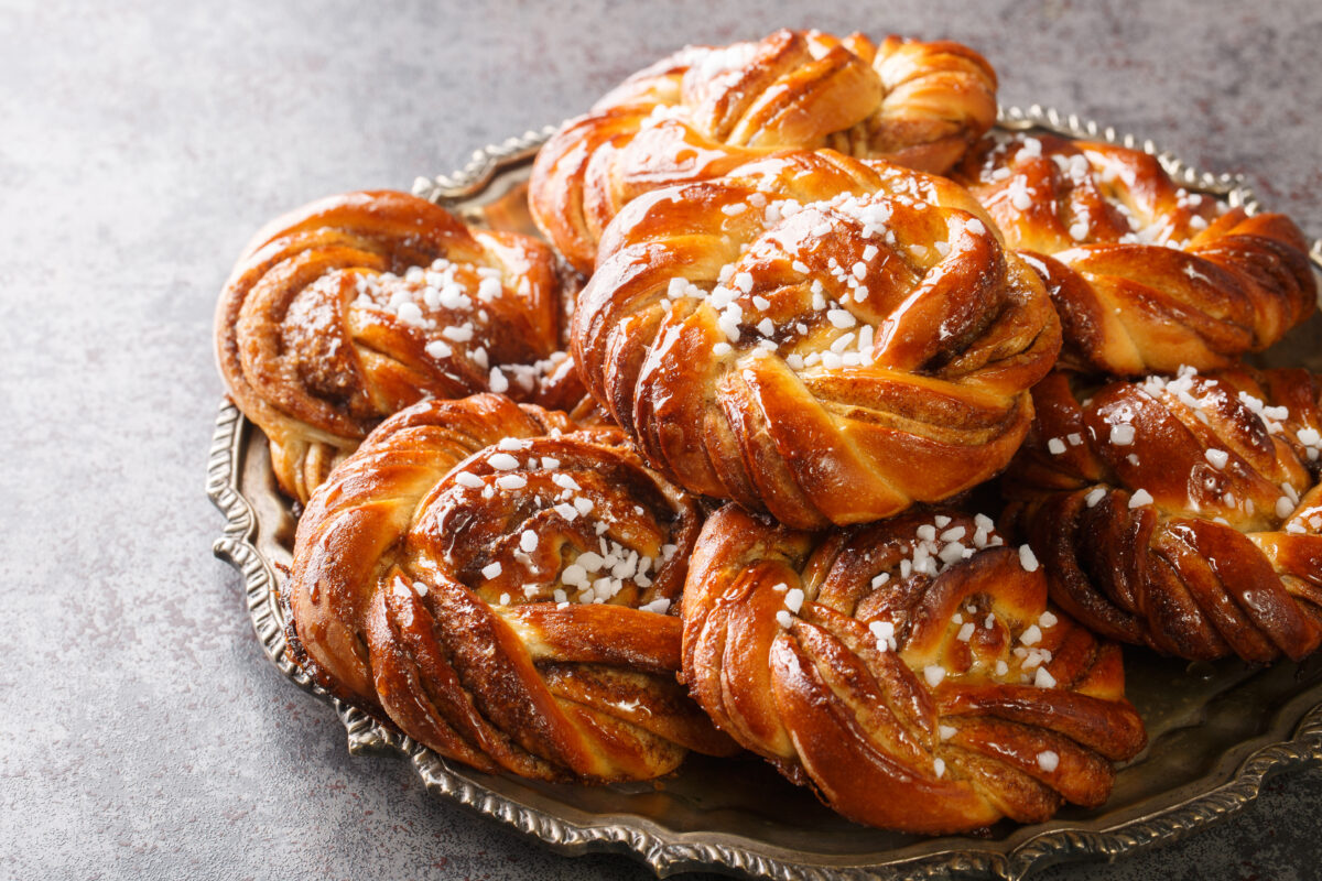 Kanelbullar or Kanelbulle is a traditional Swedish cinnamon buns flavored with cinnamon and cardamom spices and topped with pearl sugar close up on a plate. Horizontal