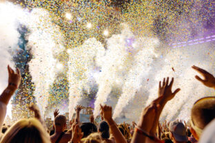 People Cheering and Dancing under Confetti at Music Festival with intense Light Show