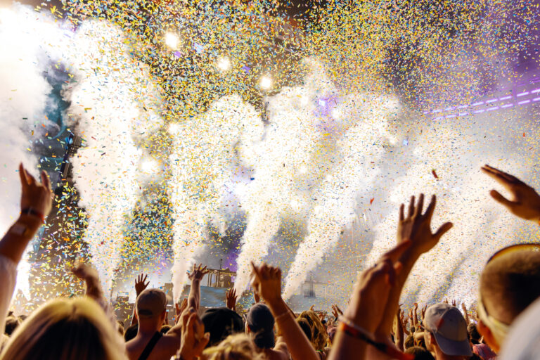 People Cheering and Dancing under Confetti at Music Festival with intense Light Show