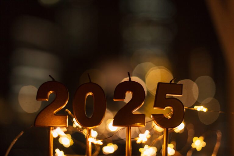 2025 festive candles stand near golden stars of lights against a city bokeh background at night. New Year 2025 and Christmas card