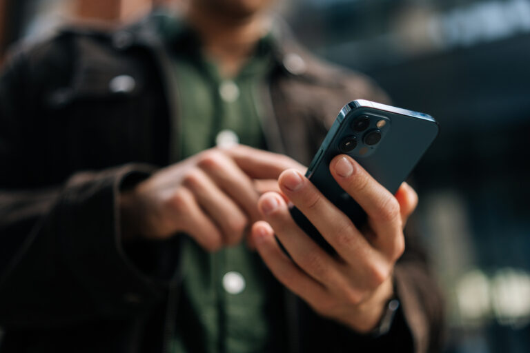 Close up hands of unrecognizable man holding and using smartphone standing on city street, browsing internet, checking social media, using mobile application.