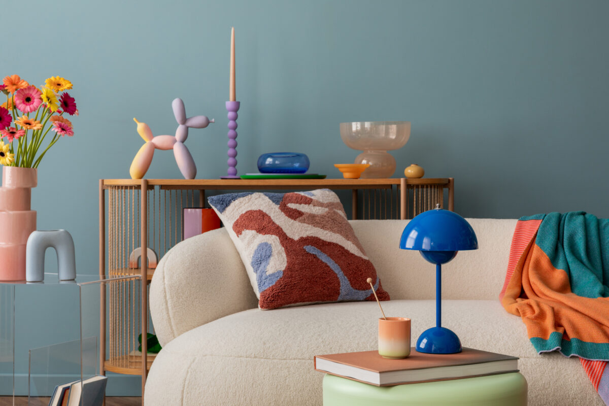 Modern decorative setup with vibrant flowers, a balloon dog sculpture, white sofa and design blue lamp. Stylish home decor.