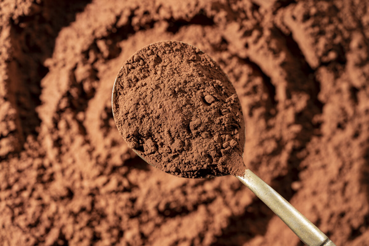 Natural dark brown cocoa powder in spoon in the background, top view, closeup. Heap of organic cacao powder
