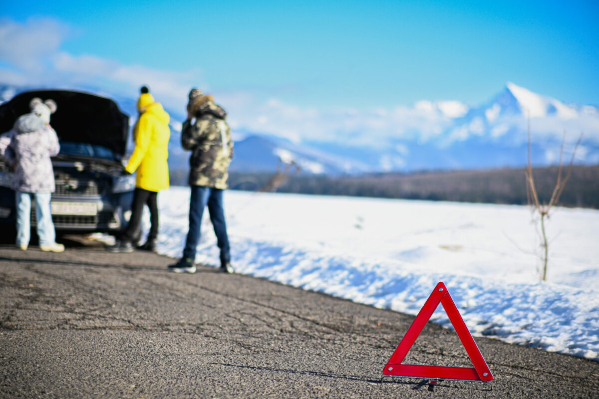Red warning triangle on road signaling car trouble for family traveling in winter