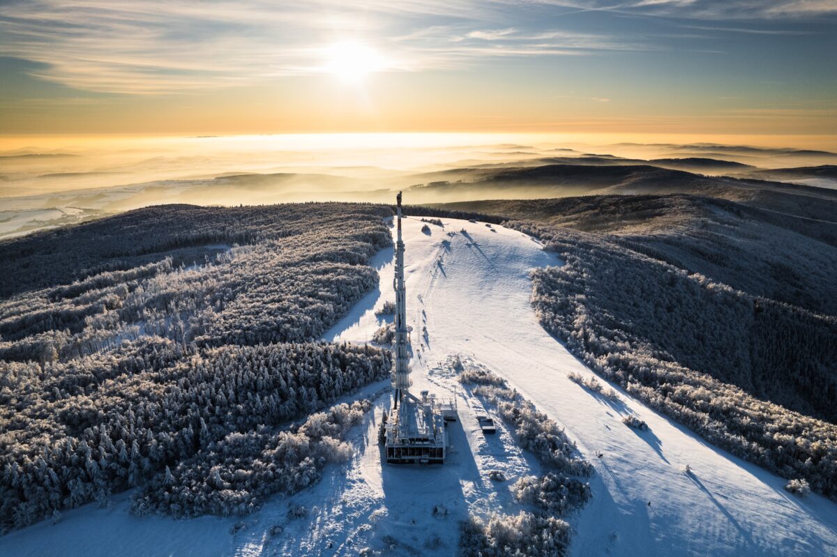 Aerial view of transmitter, cell tower surrounded by a forest during winter. Drone view of snowy landscape, christmas holidays.