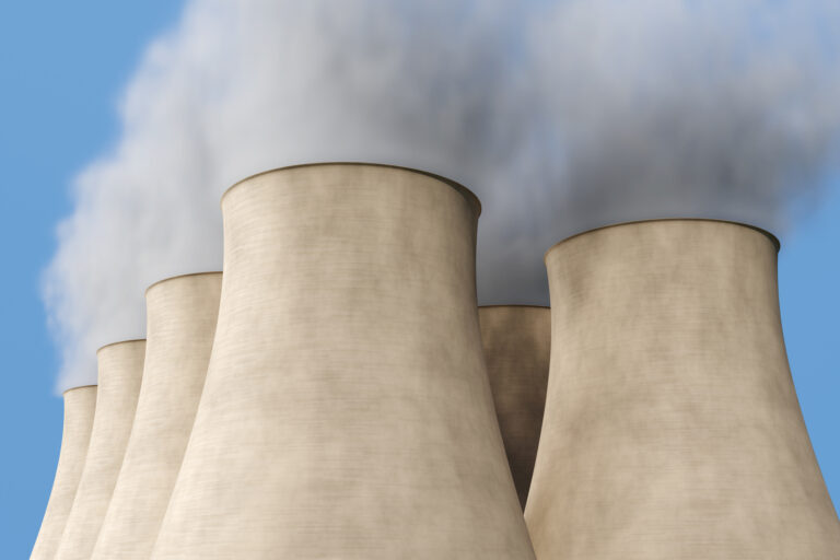 Cluster of cooling towers of a nuclear power plant emitting smoke under blue sky. Illustration of the concept of energy crisis, nuclear fission and clean energy