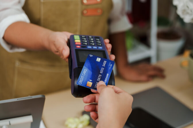 Customer holding credit card inserting into payment terminal held by asian senior florist inside flower store representing contactless cashless transaction for small flower business