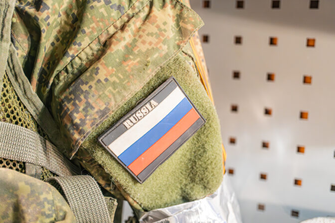 Close up image of Russian military arm, featuring camouflage pattern and a tricolor patch light blue, white, red similar to the Russian flag Realistic depiction with soft shadows under ambient lig