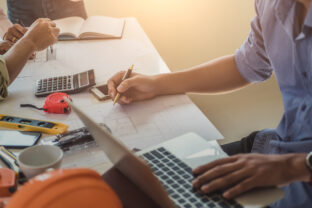 Close up of civil male engineer asian working on blueprint architectural project at construction site at desk in office.