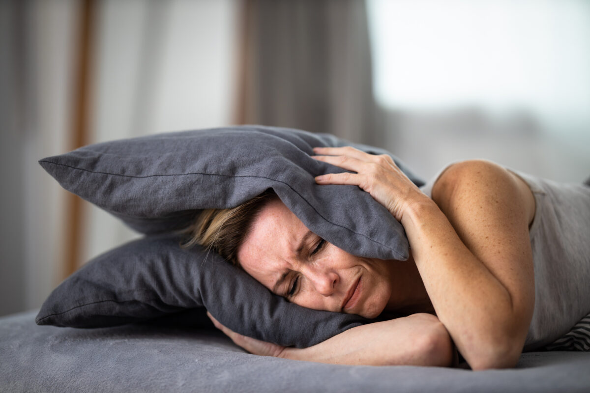 Sleepless lady covering ears with pillow