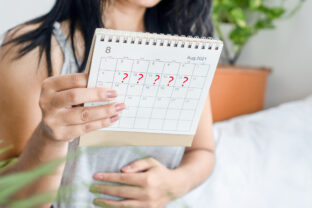 Woman hand holding calendar with question mark waiting for late blood period, amenorrhea concept