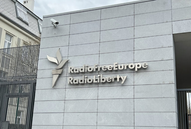 Sign "Radio Free Europe Radio Liberty" on gray building. RFE RL - international non profit broadcasting organization funded by the United States government. Headquarters in Prague - April 14, 2025.