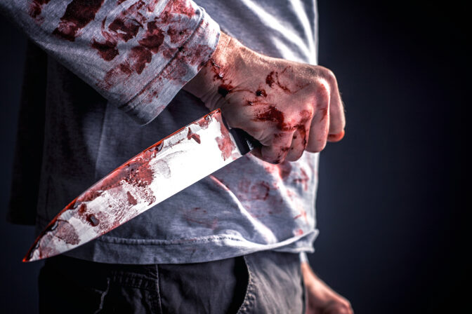 Midsection Of Murderer Holding Blooded Knife Against Black Background