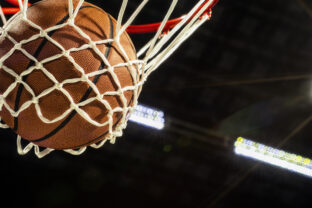Looking up at the bottom of a basketball falling through the net with arena lights in the background