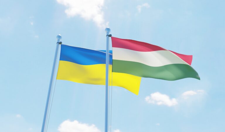 Hungary and Ukraine, two flags waving against blue sky