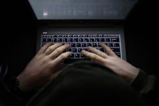 Person with a hoody typing at a computer in the dark. Suspicious online behavior